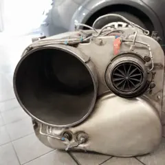Metalowy element układu wydechowego, prawdopodobnie turbosprężarka lub katalizator, leży na podłodze. Brak DPF może skutkować mandatem.