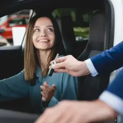 Uśmiechnięta kobieta odbiera kluczyki do samochodu. To symboliczny moment wycofania samochodu z firmy i jego darowizna.