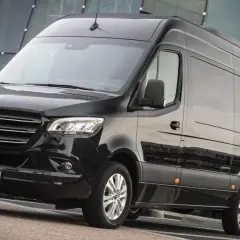 Czarny Mercedes-Benz Sprinter, jeden z najlepszych samochodów dostawczych, zaparkowany przed nowoczesnym budynkiem.