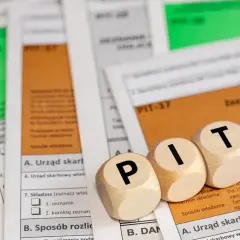Drewniane klocki z literami PIT leżą na dokumentach podatkowych. Kiedy można sprzedać auto i rozliczyć PIT?