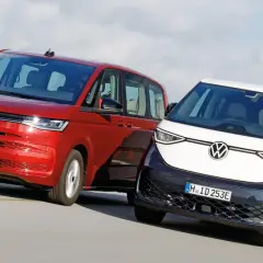 Dwa minivany Volkswagen: czerwony i dwukolorowy, jadące po drodze.