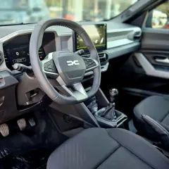 Wnętrze Dacia Bigster: kierownica z logo, ekran multimediów, dźwignia zmiany biegów i czarne siedzenia.