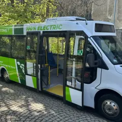 Nowy, zielono-biały bus elektryczny "Automety" z napisem "100% ELECTRIC" stoi na bruku.