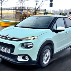 Jasnozielony Citroën C3, jeden z francuskich marek samochodów, jedzie po mokrej drodze.