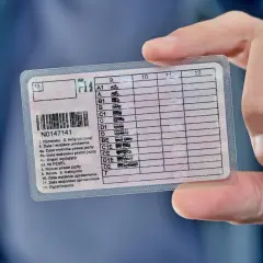 Prawo jazdy z zaznaczonymi kategoriami, w tym kod na okulary. Dokument jest trzymany przez palce.