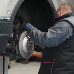 Mechanik sprawdza żywotność klocków hamulcowych przy tarczy hamulcowej samochodu na podnośniku.