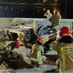 Strażacy pracują przy wraku żółtego samochodu po wypadku Patryka Peretti. Auto jest mocno zniszczone, leży na boku.