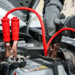 Rękawiczki pokazują, jak podłączyć kable rozruchowe do akumulatora samochodowego. Czerwone zaciski są podłączone do biegunów.