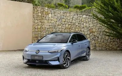 Niebieski Volkswagen ID.7, następca Passata, zaparkowany przed kamiennym murem.