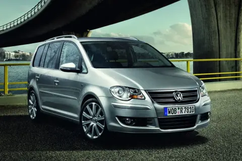 Srebrny, bezawaryjny minivan Volkswagen Touran stoi nad wodą pod mostem.