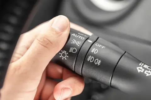 Dłoń reguluje przełącznik świateł w samochodzie, wybierając tryb AUTO lub mijania światła.