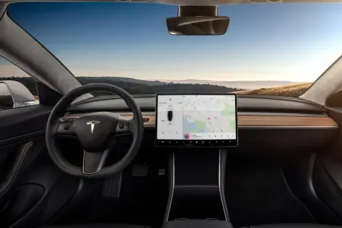 Wnętrze Tesla Model S z dużym ekranem dotykowym, kierownicą i widokiem na krajobraz za oknem.