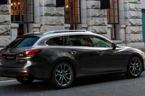 Eleganckie, ciemnoszare kombi Mazda 6, największe kombi na rynku, parkuje przed kamienną fasadą.