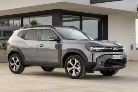Szary Dacia Duster, jeden z najlepszych aut do gazu, parkuje przed nowoczesnym budynkiem.