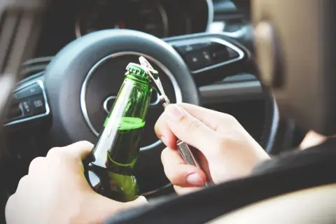 Ręce otwierają butelkę piwa za kierownicą. Nowe kary za jazdę po alkoholu powinny odstraszyć od takiego zachowania.