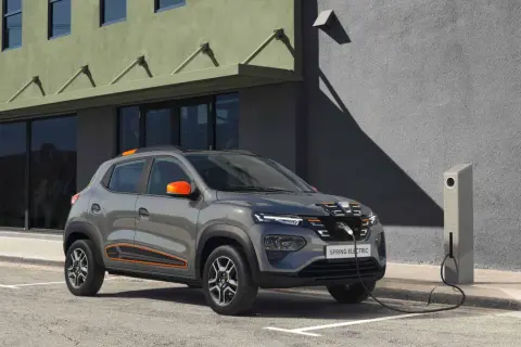 Szary Dacia Spring Electric, z pomarańczowymi akcentami, podłączony do ładowarki. Idealne wymiary do miasta.