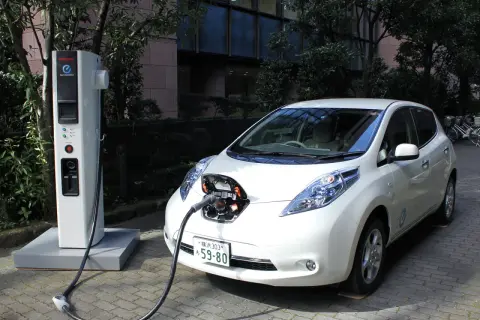 Biały Nissan Leaf podłączony do ładowarki. To przyszłość, czyli serwis samochodów elektrycznych.
