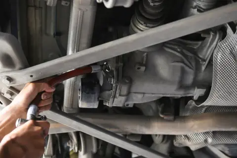 Wymiana oleju w tylnym moście. Mechanik używa wężyka do uzupełnienia płynu.