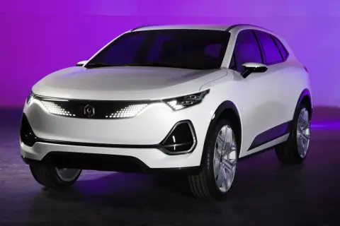 Białe, nowoczesne polskie auto elektryczne z futurystycznymi światłami LED, prezentowane na tle fioletowej ściany.