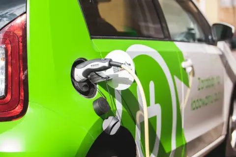 Zielony samochód elektryczny podłączony do ładowania. Sprawdź aktualne ceny ładowania samochodów elektrycznych.