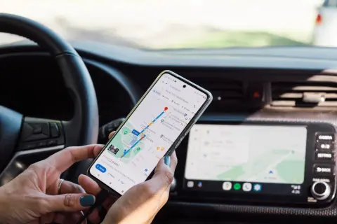 Ręce kierowcy trzymają telefon z nawigacją, co stanowi niebezpieczne używanie telefonu podczas jazdy.