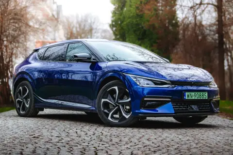 Niebieska Kia EV6 na testowej drodze, wśród drzew. Elegancki design i nowoczesne linie podkreślają jej elektryczny charakter.