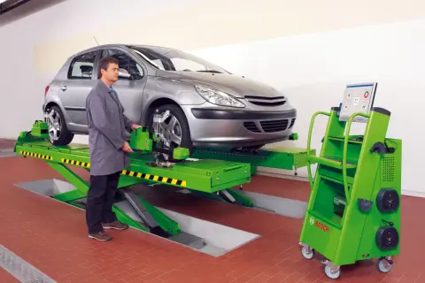 Mechanik sprawdza zbieżność kół samochodu na podnośniku, używając zaawansowanego sprzętu do pomiaru geometrii.