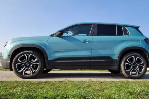 Turkusowy Jeep Avenger, najładniejszy suv, prezentuje się stylowo na tle błękitnego nieba i zielonej trawy.