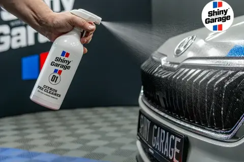 Ręka rozpyla preparat Shiny Garage Citrus Pre Cleaner na grill samochodu, rozpoczynając jego mycie.