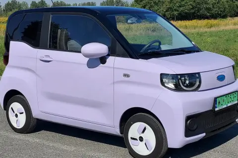 Fioletowy samochód elektryczny na tle łąki. Czy wady samochodów elektrycznych są widoczne w jego kompaktowej budowie?