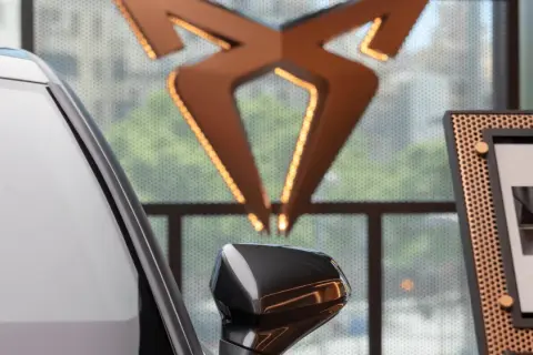 Biały samochód i logo producenta Cupra. Obok zdjęcie nowego modelu Cupra Leon PHEV.