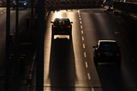 Zachód słońca rzuca długie cienie na drogę, gdzie dwa samochody jadą jak piraci drogowi, omijając przeszkody.