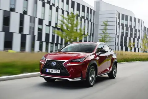 Czerwony Lexus NX, uznawany za najbardziej ekonomiczny SUV, jedzie przed nowoczesnym budynkiem.