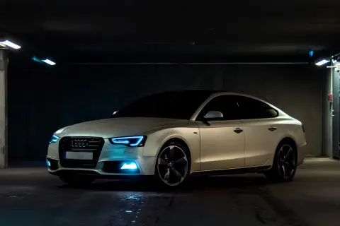 Białe Audi z niebieskimi światłami w garażu. Samochód powyżej 150 tys. a koszty utrzymania? Warto rozważyć.