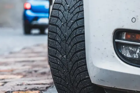 Białe auto z oponami zimowymi na mokrej nawierzchni. Niebezpieczna jazda na letnich oponach w zimie to ryzyko.