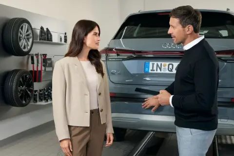 Klientka rozmawia z pracownikiem serwisu Audi o akcjach serwisowych. Na ścianie widoczne opony i akcesoria.