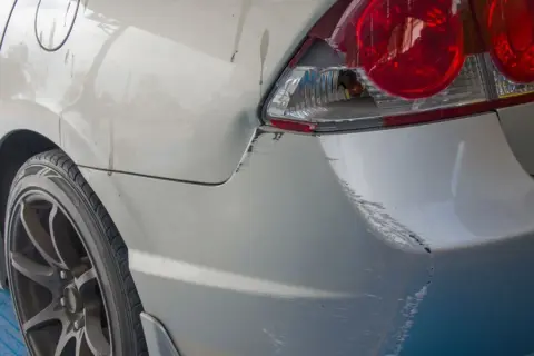 Uszkodzony tył samochodu po parkingowej stłuczce. Wgniecenie i liczne zarysowania lakieru, typowe dla szkody w leasingu.
