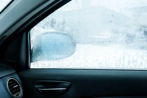 Widok z wnętrza auta na zaparowane szyby. Krople wody na szybie utrudniają widoczność drogi i lusterka bocznego.