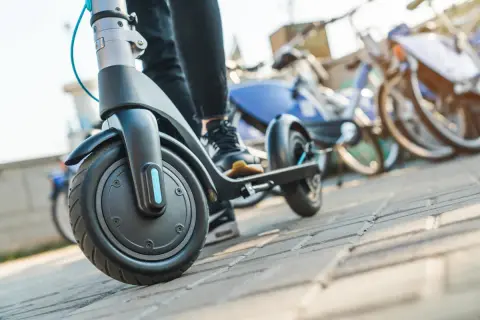 Osoba na hulajnodze elektrycznej, gotowa do jazdy. W tle stoją rowery miejskie. Przepisy hulajnoga elektryczna to ważna sprawa.