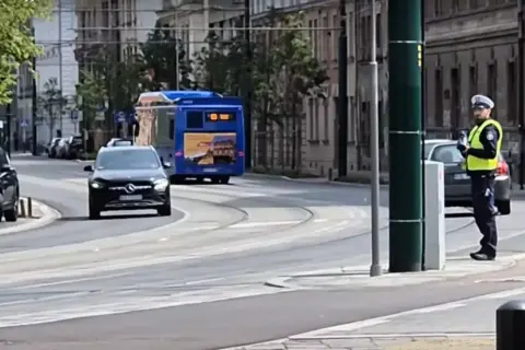 Policjant w kamizelce odblaskowej stoi przy ulicy, kontrolując ruch. Czy radiowóz musi być widoczny, by zapewnić bezpieczeństwo?