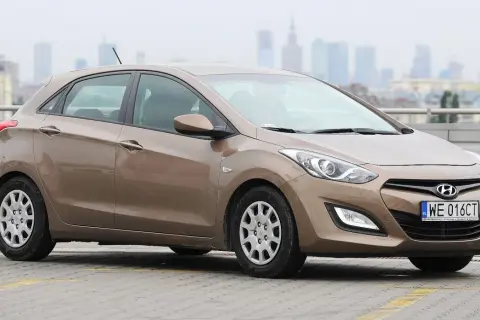 Brązowy Hyundai i30, jedna z popularnych generacji tego modelu, zaparkowany na tle miejskiej panoramy.