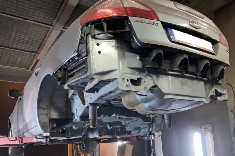 Ford Mondeo na podnośniku, przygotowany do piaskowania podwozia. Widać gołe elementy konstrukcyjne i usunięty zderzak.