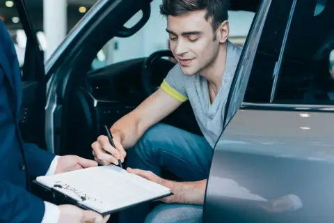 Mężczyzna w samochodzie podpisuje umowę. Chcesz wiedzieć, jak sprawdzić, czy auto jest w leasingu? Dokumenty są kluczem.