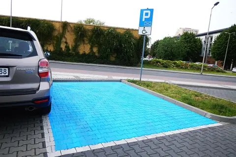 Niebieski, specjalny obszar do parkowania na miejscu dla niepełnosprawnych. Obok znak drogowy P i symbol wózka inwalidzkiego.