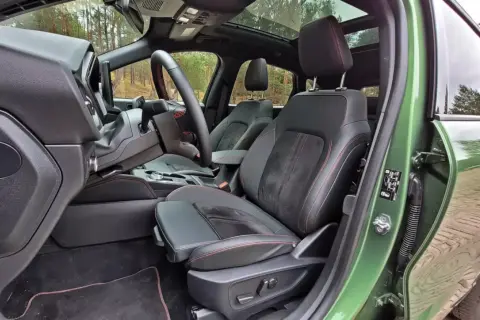 Wnętrze Ford Kuga z czarną tapicerką i czerwonymi przeszyciami. Widok na fotel kierowcy, deskę rozdzielczą i fragment dachu panoramicznego.
