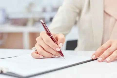 Dłoń podpisuje dokument, być może weksel gwarancyjny, na białym biurku.