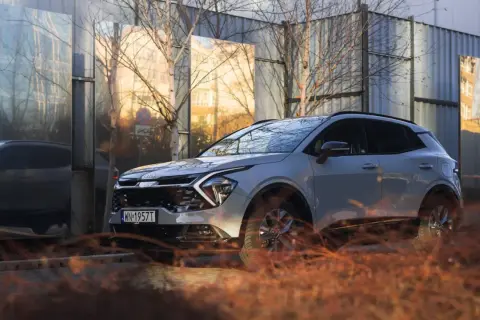 Nowe auto typu SUV w jasnym kolorze, zaparkowane obok lśniących paneli odbijających otoczenie.