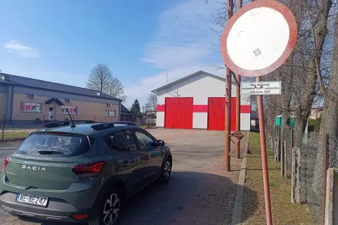 Zielony Dacia Sandero stoi przed remizą OSP. Znak zakazu ruchu z tabliczką "Nie dotyczy pojazdów OSP i pojazdów członków OSP" ostrzega przed mandatem.