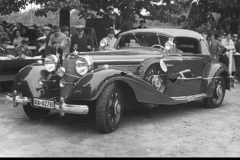 Elegancki, zabytkowy pierwszy mercedes z lat 30. XX wieku, z widoczną tablicą rejestracyjną IIA-42781, otoczony przez ludzi.
