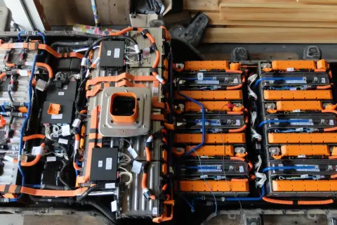 Widok z góry na budowę baterii samochodu elektrycznego, z widocznymi modułami ogniw, pomarańczowymi przewodami i czarnymi skrzynkami sterującymi.